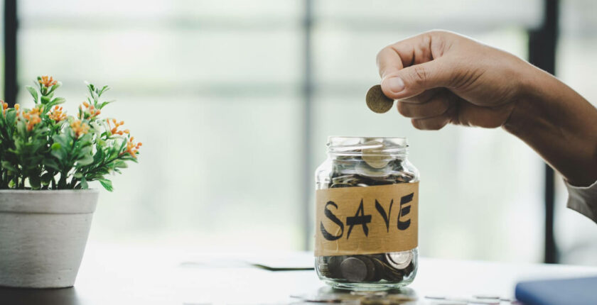 glass jar that says save and a person putting coins inside